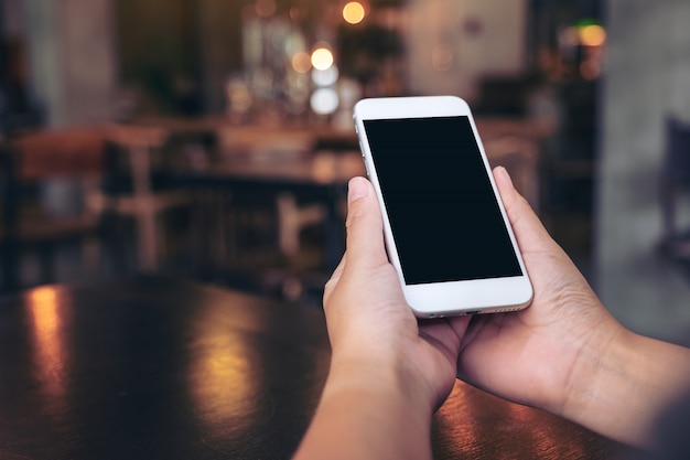 Hands holding white mobile phone with blank black screen in vintage cafe