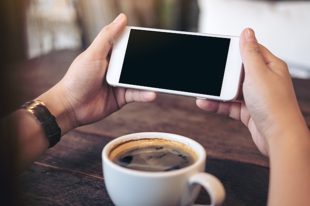 hands holding white mobile phone with blank black screen for watching and playing games 