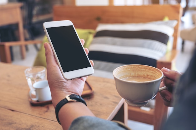 カフェでコーヒーを飲みながら空白の画面で白い携帯電話を持っている手