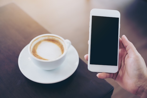 Hands holding white mobile phone with blank white screen