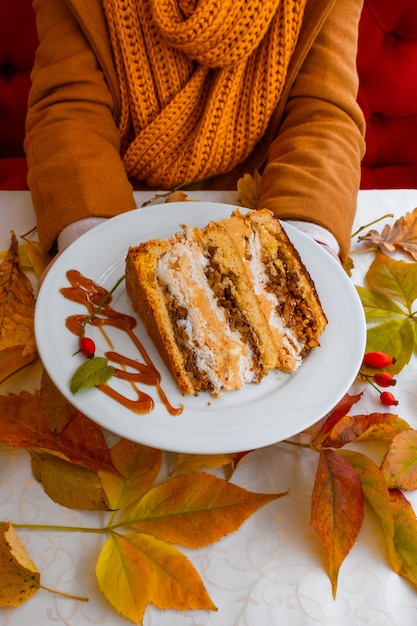 hands holding white plate cake autumn leaves