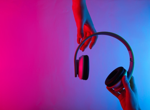 Hands holding wireless stereo headphones with neon blue-pink gradient light