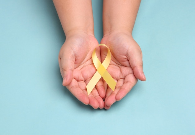 hands holding yellow gold ribbon on blue background