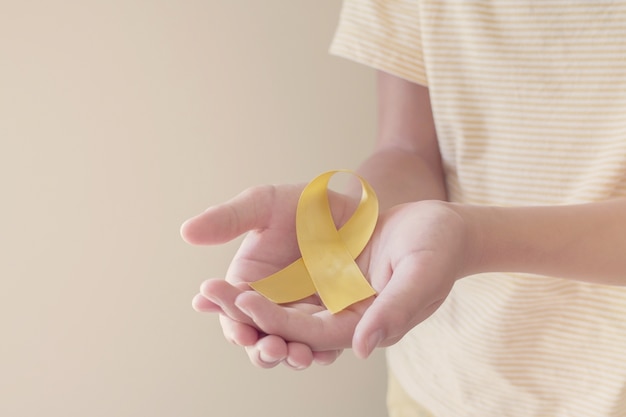 Mani che tengono il nastro dell'oro giallo, consapevolezza del sarcoma, consapevolezza del cancro infantile, concetto di giornata mondiale per la prevenzione del suicidio