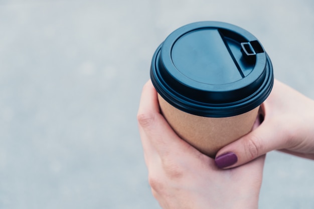 Hands holds coffee in brown cardboard cup with black cap 