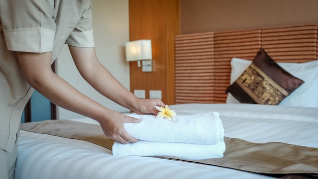 Hands of hotel maid putting plumeria flower and towels on the bed in the luxury hotel room