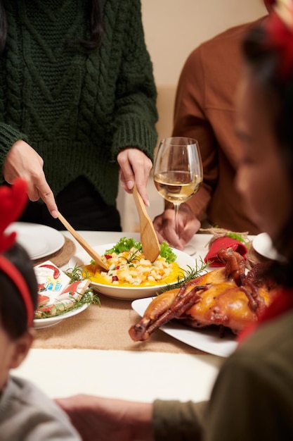 Hands of housewife putting salad in plates of guests at christmas dinner party