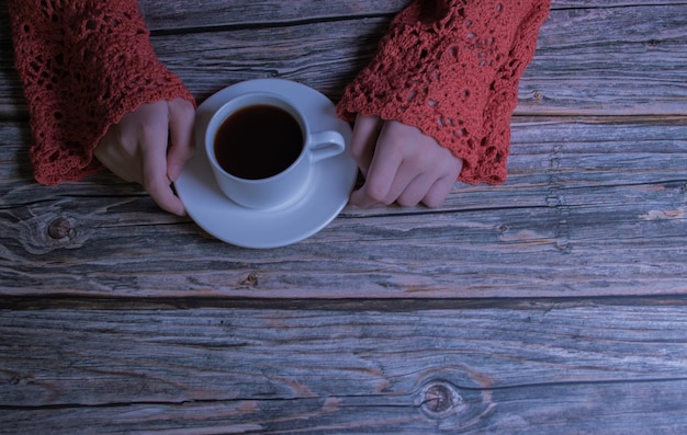 Фото Руки в вязаном ажурном свитере, чашка кофе на деревянном столе