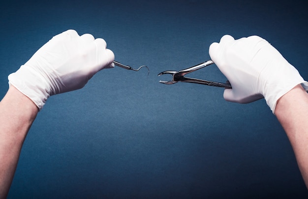 Фото Руки в перчатках, держа стоматологические инструменты хирургии на синем фоне
