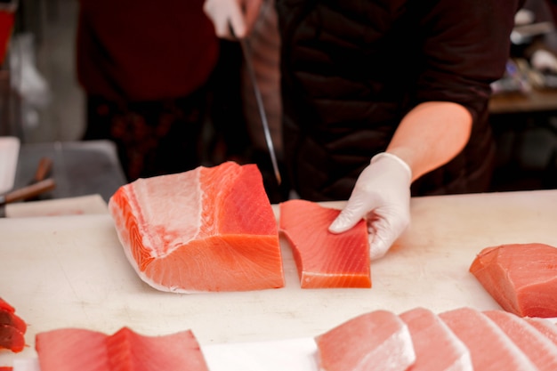 Photo hands of japanese chef using chef knife sliced piece of fresh tuna fish for sell to customer in morning fish market, japan.