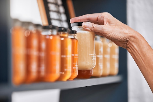 オーガニック小売店での在庫チェック製品の価格設定またはラベル付けのための手の瓶と蜂蜜の棚中小企業の管理または販売のための健康的なガラス食品の市場広告での手