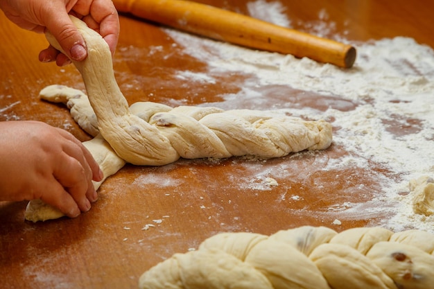 The hands of a Jewish woman weave a challah in the form of a pigtail for Shabbat on a wooden table