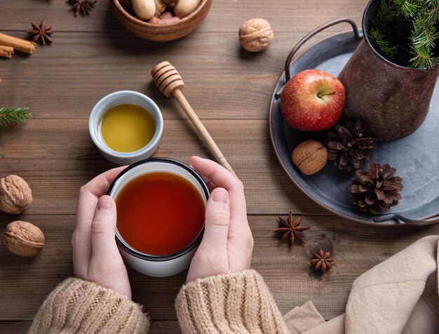 Le mani mantengono la tazza di tè aromatizzato alla mela di natale con cannella su un tavolo di legno. vista dall'alto