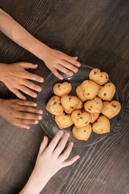 Mani di bambini che prendono biscotti fatti in casa sul tavolo mentre sono entrambi in piedi accanto al tavolo in cucina