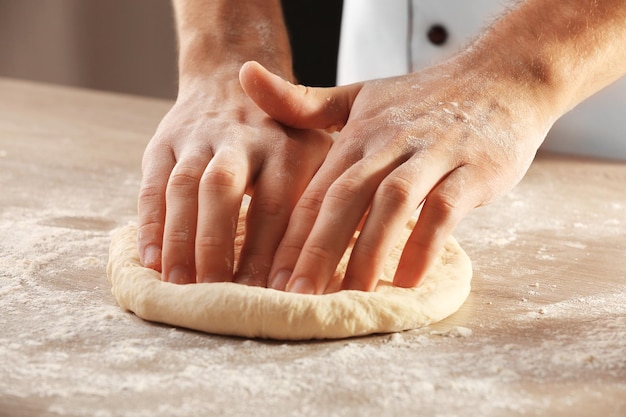 Hands kneading dough for pizza on the wooden table closeup