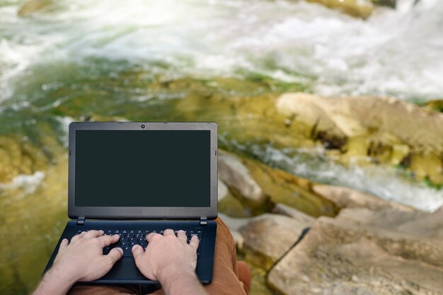 hands on the laptop keyboard on the background of a river