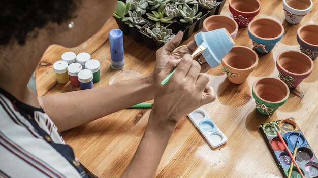 Hands of a Latin mulatto woman painting clay pots to plant succulent plants