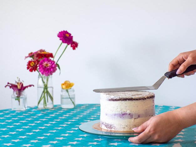 Hands level the cream with a spatula and cover the round cake