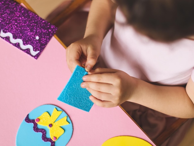 Hands of a little caucasian girl holding a blue sticker and peeling off a hat for felt eggs