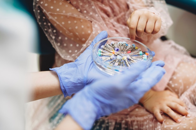 Mani della bambina che sceglie gli strumenti per la futura chirurgia dei denti mentre è seduto in una stomatologia pediatrica.