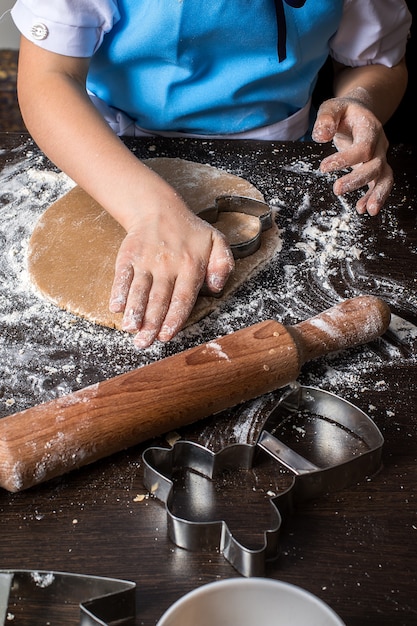 Hands of little girl sheeting dough with rolling pin.