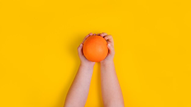 Photo hands of little girl with orange fruit on orange background top view copy space