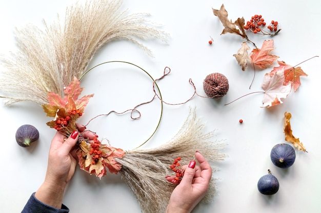 Hands making dried floral wreath from dry pampas grass and Autumn leaves Hands in sweater tie decorations to metal frame