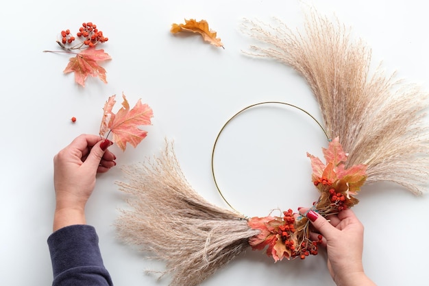 Hands making dried floral wreath from dry pampas grass and Autumn leaves Hands in sweater tie decorations to metal frame