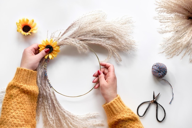 Hands making dried floral wreath from dry pampas grass and Autumn leaves Hands in sweater tie decorations to metal frame