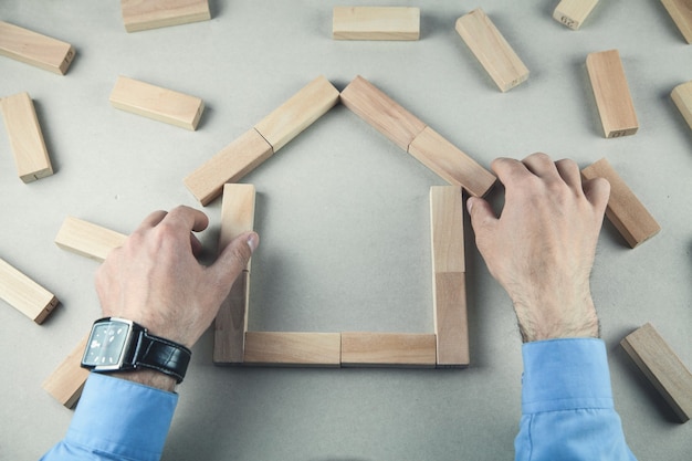 Hands making house of wooden blocks.