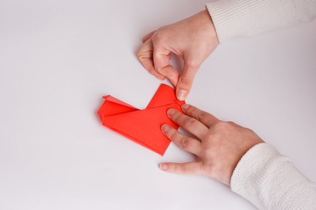 Hands making origami heart close up on white