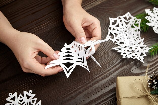 Hands making white paper snowflake on wooden table