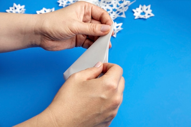 Photo hands making white paper snowflakes on blue