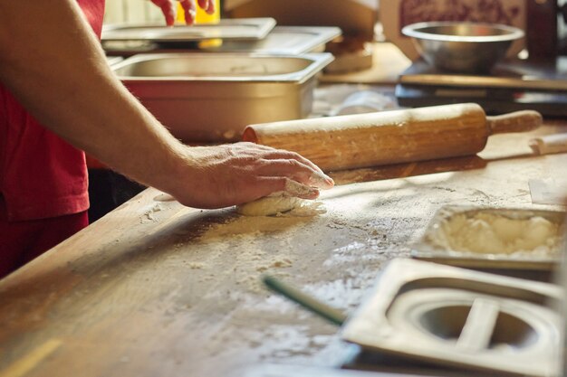 Mani del panettiere maschio con la pasta della farina che prepara alimento sulla tavola di legno