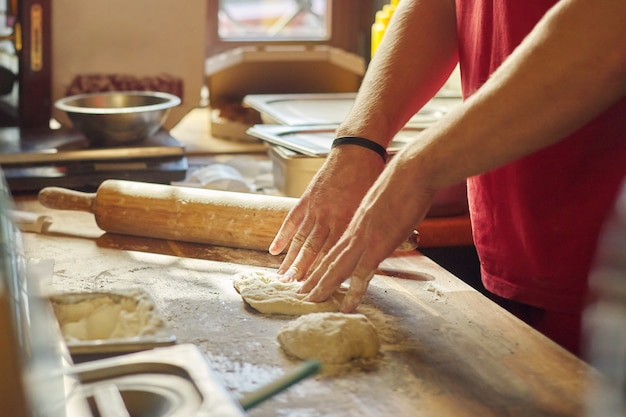 Mani del panettiere maschio con la pasta della farina che prepara alimento sulla tavola di legno