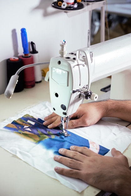 Hands of male tailor testing new silk fabric and making few stitches on sewing machine