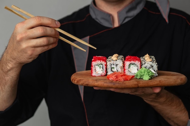 Foto mani di un cuoco unico in uniforme nera che tiene un vassoio in legno pieno di sushi