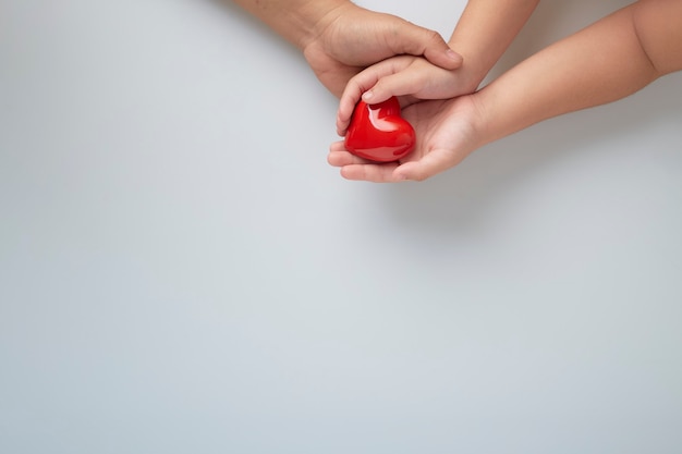 Hands of man and child with a red heart on white wall