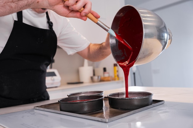 Le mani di un uomo che cucinano una torta di velluto rosso a casa aggiungendo il pan di spagna negli stampi prima di metterlo in forno lavorano a casa