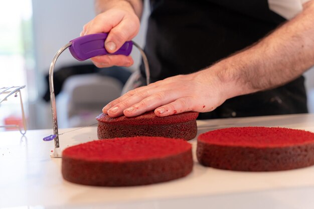 Mani di un uomo che cucina una torta di velluto rosso a casa che taglia la torta cotta a casa con una lira