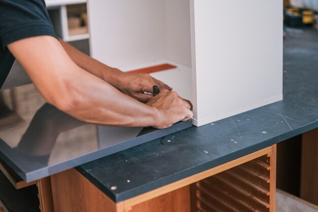 Hands of a man fixing a hinge on a surface for a kitchen