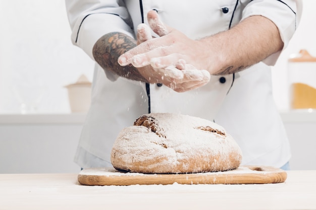 Hands of a man and fresh baked bread on a wooden table. soft light