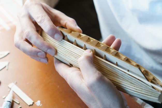 Hands of man gluing plywood details for ship model with glue holding with fingers Process of building toy ship