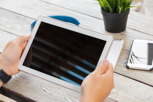 hands of a man holding tablet device over a wooden workspace table