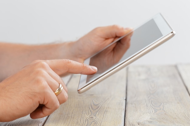 Hands of a man holding tablet device over a wooden workspace table