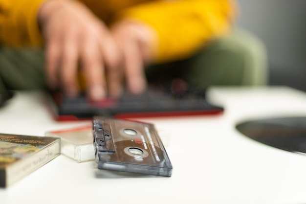 Foto le mani di un uomo che fa musica con il suo controller midi in contrasto con i vecchi vinili e le cassette da cui campiona