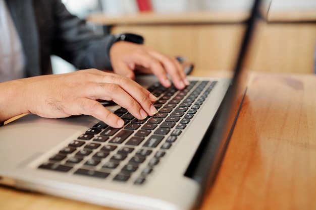 Mani dell'uomo seduto alla scrivania dell'ufficio e che programmano sul laptop o lavorano su un rapporto mensile