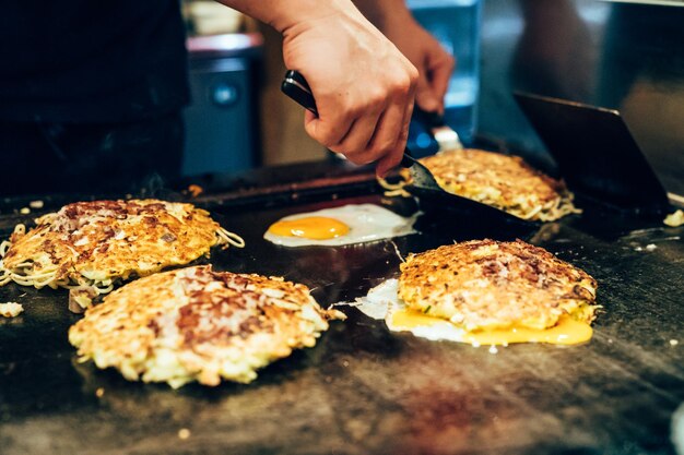 Hands of man take cooking of egg and noodles grill. Chef making delicious street food in Japanese teppanyaki restaurant. close up photo of tasty snack on hot iron plate.