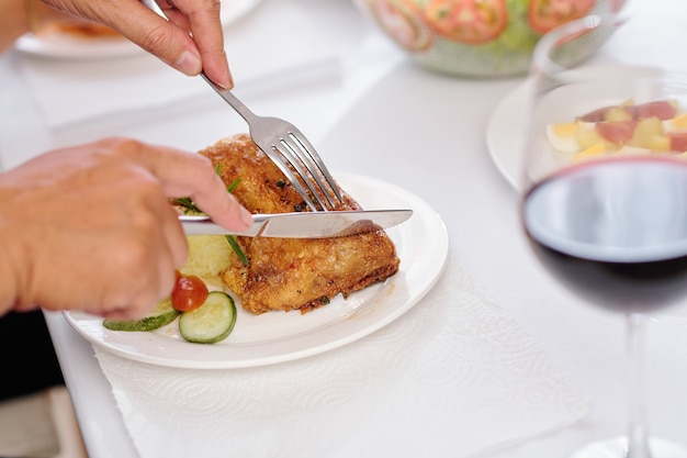 Hands of man using fork and knife when eating fried chicken at festive dinner at home