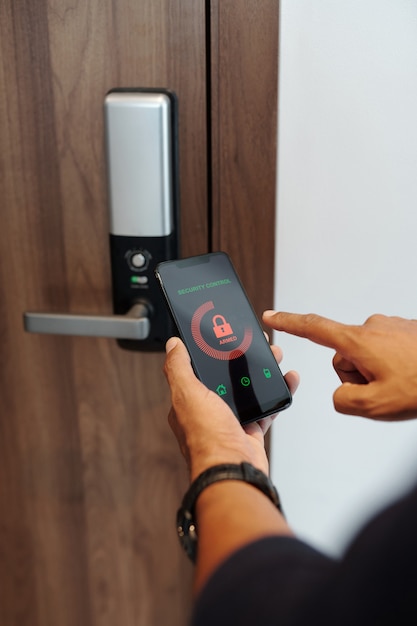 Hands man using security control application on smartphone when locking apartment door